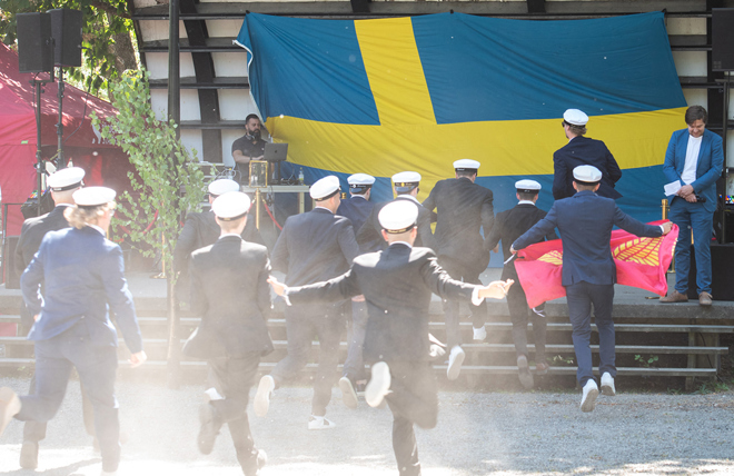Studenter springer mot scenen i Stadsparken. En svensk flagga breder ut sig bakom scenen.